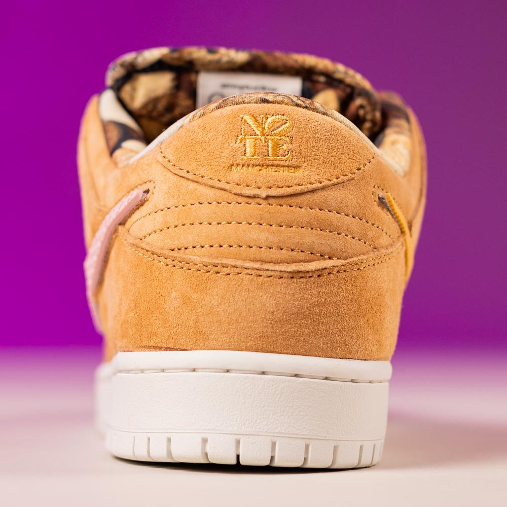 Close-up of the back of a tan suede READ BELOW the BUTTON RAFFLE Nike SB Brew and Biscuits Dunk Low with N7 TE embroidery above the white sole on a purple background. Patterned lining—ideal for your next Southside Skatepark raffle entry.