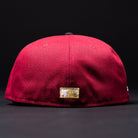 The Bloodline OG Cardinal Red Houston Astros New Era Hat 5950 Fitted is shown from the back against a black background, featuring a small embroidered gold and white patch near the bottom edge. This fitted cap by New Era blends subtle team pride with classic style.