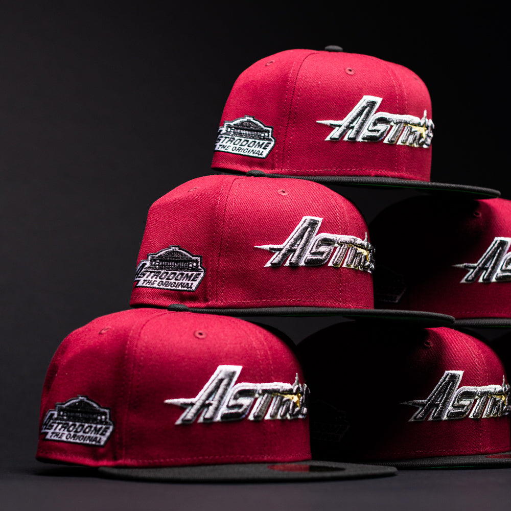 Six Bloodline OG Cardinal Red Houston Astros New Era Hat 5950 Fitted caps, adorned with both the Houston Astros and Astrodome The Original patches, are stacked in a dark setting. The hats feature Cardinal Red crowns paired with black brims and bold white, gold, and silver embroidered lettering and logos.