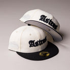 Two Straight Outta Southside OG Chrome Black Houston Astros New Era 5950 Fitted caps are stacked, featuring white panels with black brims. Each cap displays “Astros” in black gothic-style lettering on the front and a gray embroidered side patch. The iconic gold sticker is visible on one brim, highlighting this classic choice for Houston Astros fans.
