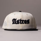 Introducing the Straight Outta Southside OG Chrome Black Houston Astros New Era Hat 5950 Fitted: a cream and black fitted cap by New Era featuring ‘Astros’ in black Old English lettering on the front, shown against a plain background—an ideal pick for any Houston Astros fan.