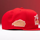 A bright red H Town South Houston Astros New Era Hat 5950 Fitted, featuring tan embroidered patches with stylized text and logos on the front and side, inspired by the Houston Astros. The backdrop is a gradient of red shades, adding a bold touch reminiscent of classic New Era designs.
