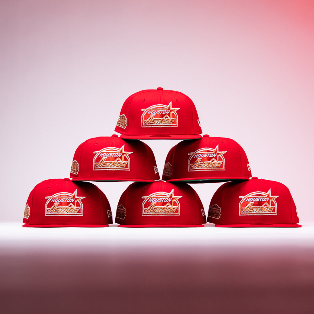 Six H Town South Houston Astros New Era Hat 5950 Fitted caps in red are stacked in a pyramid shape on a white surface, set against a gradual pink-to-white background, with prominent Astros logos displayed on the front of these iconic fitted hats.