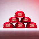 Six H Town South Houston Astros New Era Hat 5950 Fitted caps in red are stacked in a pyramid shape on a white surface, set against a gradual pink-to-white background, with prominent Astros logos displayed on the front of these iconic fitted hats.