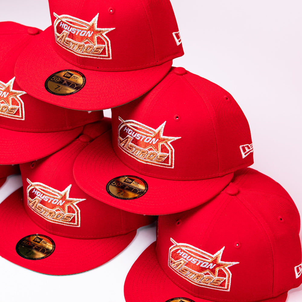 Several red H Town South Houston Astros New Era Hat 5950 Fitted caps are stacked together, each displaying the team’s logo on the front and gold sizing stickers on the bills.