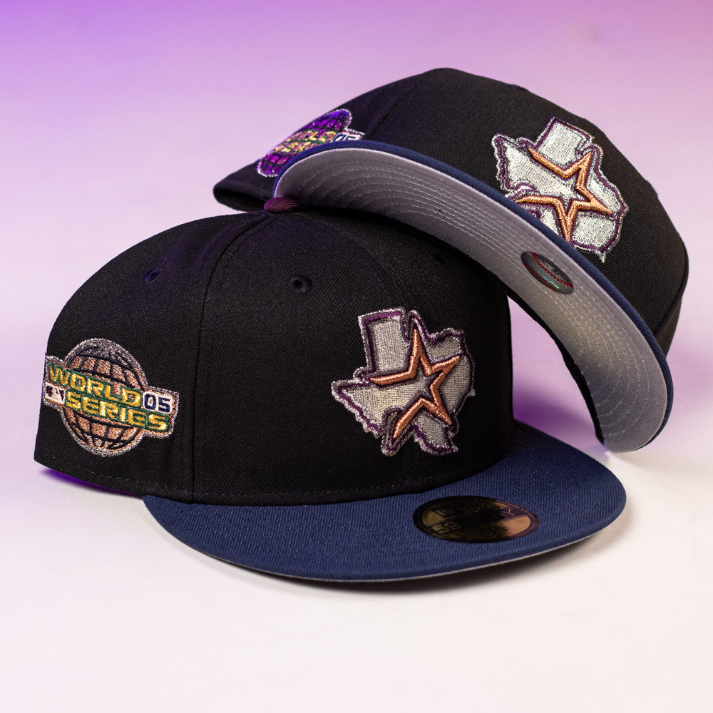 Two black and blue Masterpiece WS05 Houston Astros New Era 5950 Fitted hats with Texas-shaped star front patches and a World Series side patch, shown on a light surface with a purple gradient background. Perfect for Astros fans.