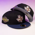 Two black and blue Masterpiece WS05 Houston Astros New Era 5950 Fitted hats with Texas-shaped star front patches and a World Series side patch, shown on a light surface with a purple gradient background. Perfect for Astros fans.
