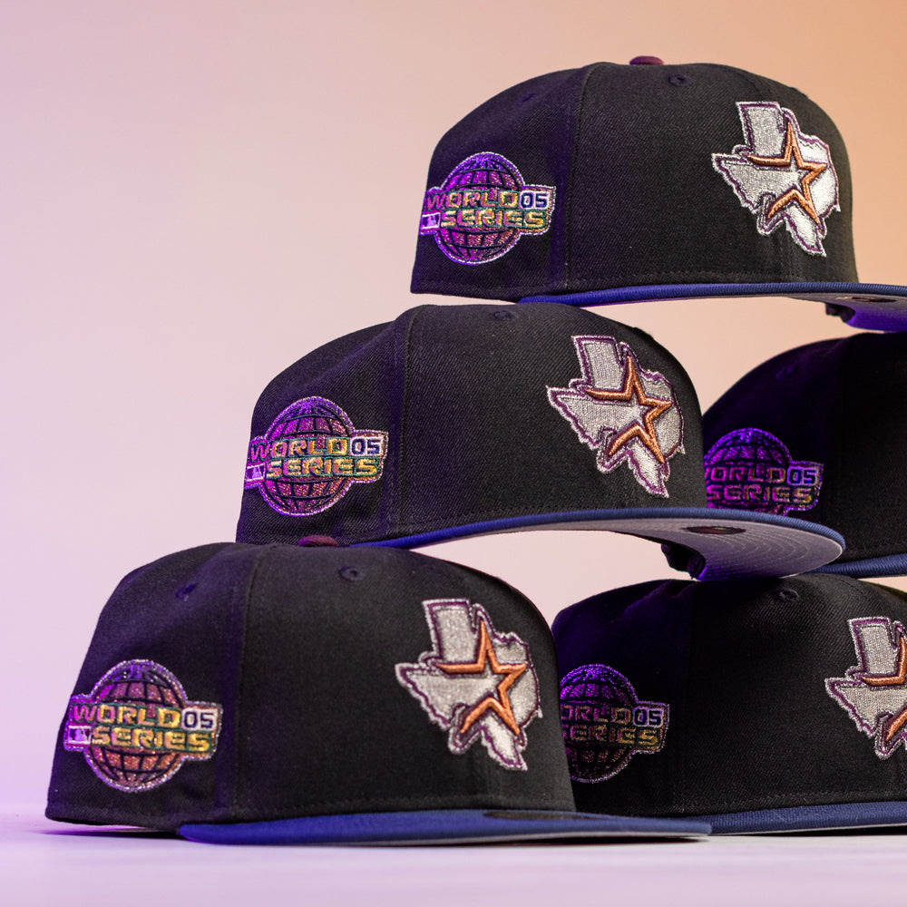 The Masterpiece WS05 Houston Astros New Era Hat 5950 Fitted features black caps with embroidered Texas-shaped patches, a star, and World Series logos, displayed on a gradient beige and purple background.