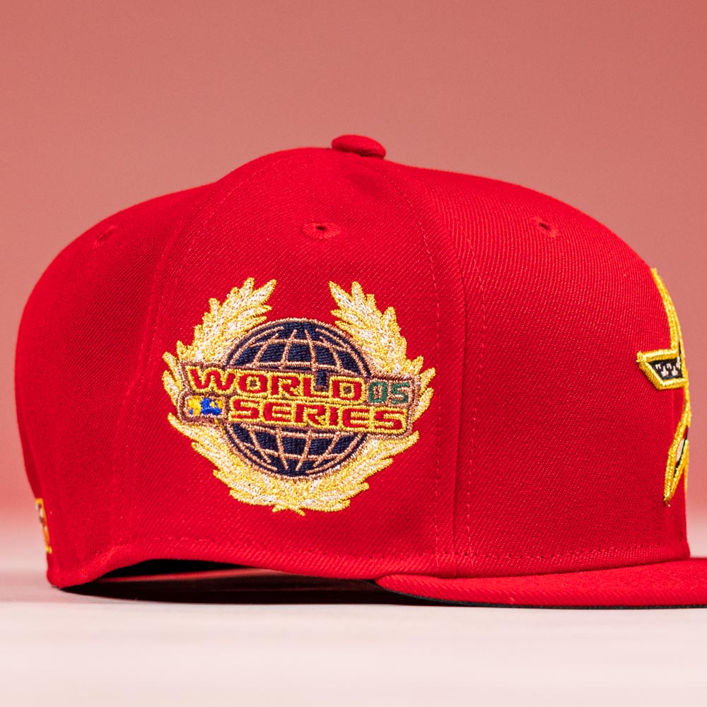 The Crest Lo 2.0 Houston Astros New Era Hat 5950 Fitted by New Era is red, with a gold and blue World Series globe and laurel patch on the side, shown against a pink background.