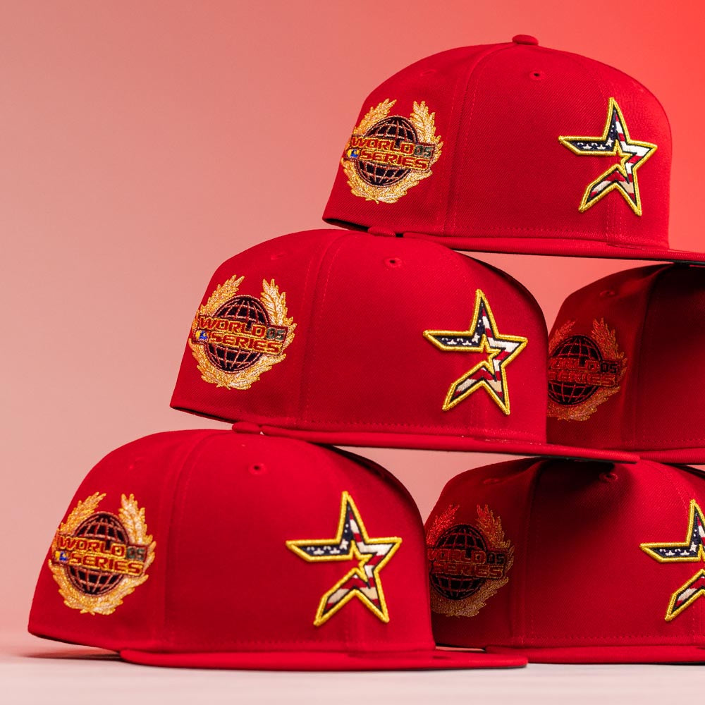 Six Crest Lo 2.0 Houston Astros New Era 5950 Fitted hats in red are stacked in two piles against a pink and red background, each featuring a gold and black World Series patch and star logo embroidered on the front and side.