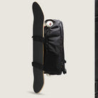 The Obstacle Skatepack Backpack VN0A3I696ZC1 Black Ripstop by Vans Skateboarding, shown in profile with side straps securing a vertically attached skateboard and wheels visible above, is ideal as a skatepack or laptop backpack.