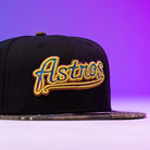 The Oil Spill WS05 Houston Astros New Era Hat 5950 Fitted features "Astros" embroidered in gold, blue, and orange script on black fabric with a purple gradient backdrop—a must-have for dedicated Houston Astros fans.