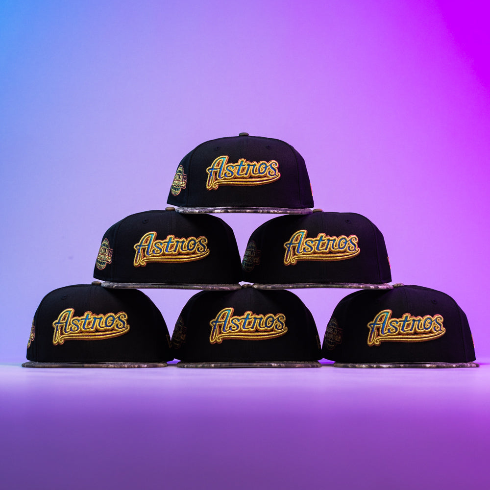 Six Oil Spill WS05 Houston Astros New Era Hat 5950 Fitted caps by New Era, each with vibrant embroidered logos, are pyramid-stacked against a vivid purple and blue gradient background.