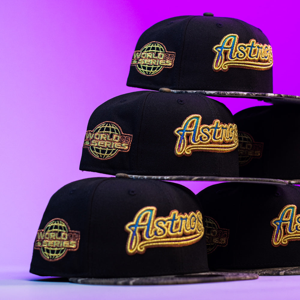 Four Oil Spill WS05 Houston Astros New Era Hat 5950 Fitted caps are stacked pyramid-style against a purple background, each featuring a gold World Series patch and a yellow Astros logo on the front.