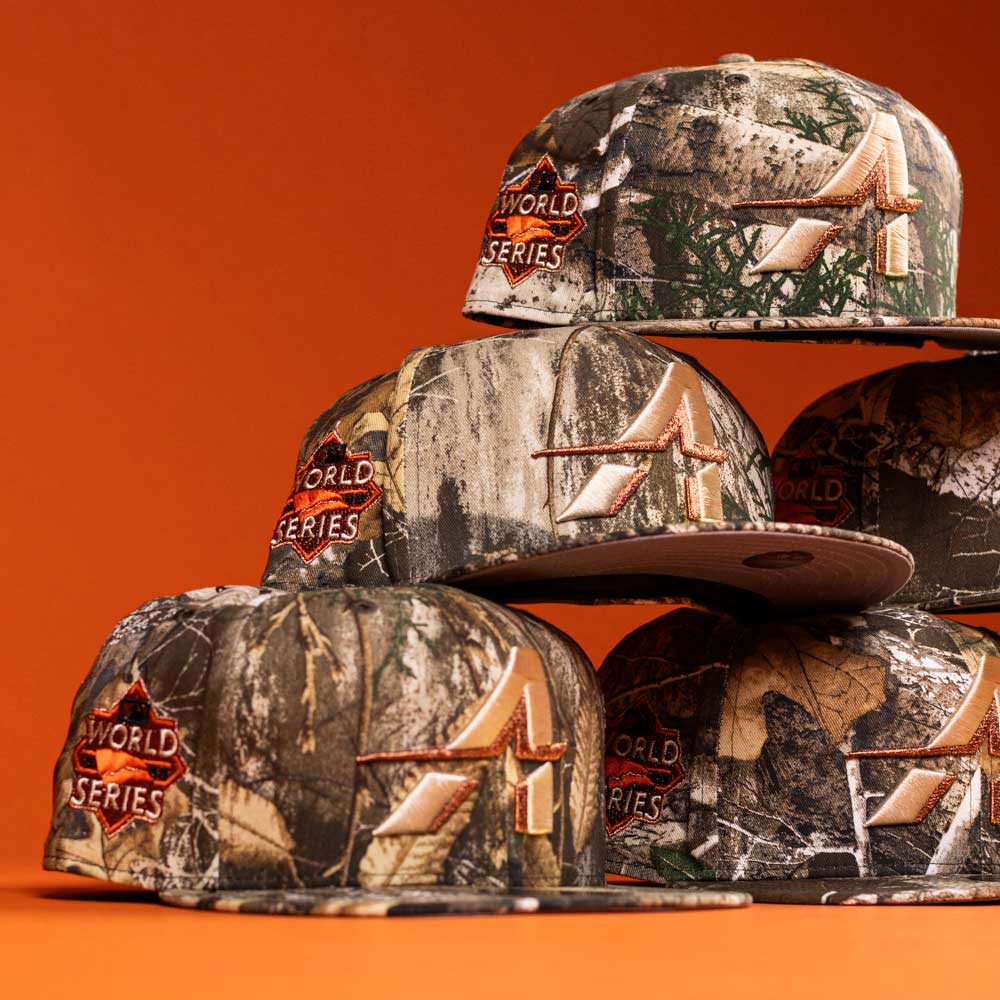 Four Panhandle Real Tree Orange Houston Astros New Era 5950 Fitted hats, featuring camouflage fabric and orange “A” logos, are stacked against an orange background.