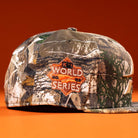 The Panhandle Real Tree Orange Houston Astros New Era 5950 Fitted hat features camo print and an orange World Series patch, displayed against an orange background.