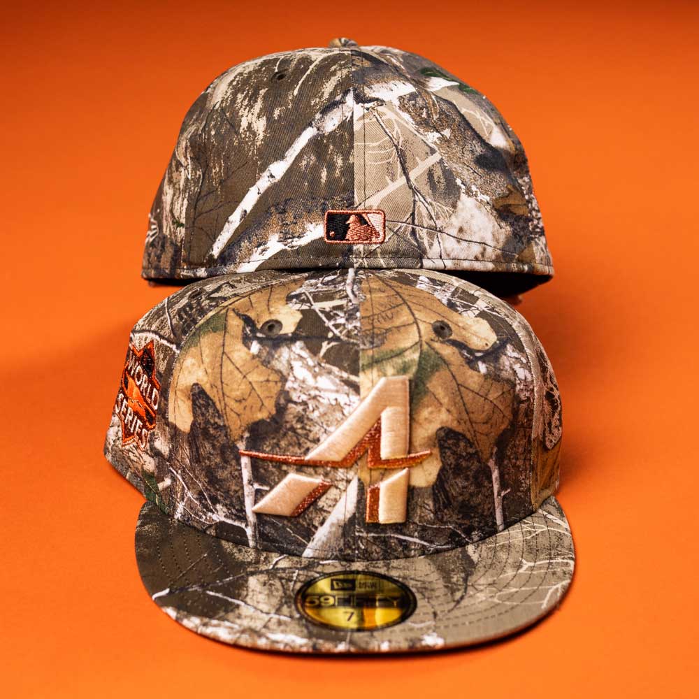 Two Panhandle Real Tree Orange Houston Astros New Era 5950 Fitted hats are on an orange surface. One shows the front, featuring the team logo, while the other displays the back and side patch details.