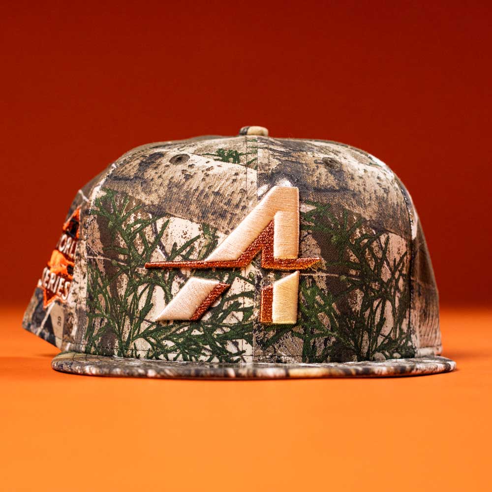 The Panhandle Real Tree Orange Houston Astros New Era 5950 Fitted hat features a camouflage design and an embroidered stylized A logo on the front, shown against an orange background.