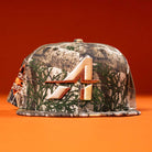 The Panhandle Real Tree Orange Houston Astros New Era 5950 Fitted hat features a camouflage design and an embroidered stylized A logo on the front, shown against an orange background.