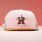 The Anglera 17WS Pink Trucker Houston Astros New Era Hat 5950 Fitted features pink and beige mesh, a brown brim, and a large embroidered H over a star on the front. It's shown against a pink background.