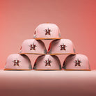 Six 17WS Pink Trucker Houston Astros New Era Hat 5950 Fitted caps are stacked in a pyramid on a pink background, each featuring the Astros’ star logo on the front.