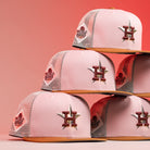Six 17WS Pink Trucker Houston Astros New Era Hat 5950 Fitted caps, featuring the Astros H logo and World Series Champions patch, are stacked in a pyramid against a pink and red gradient background.