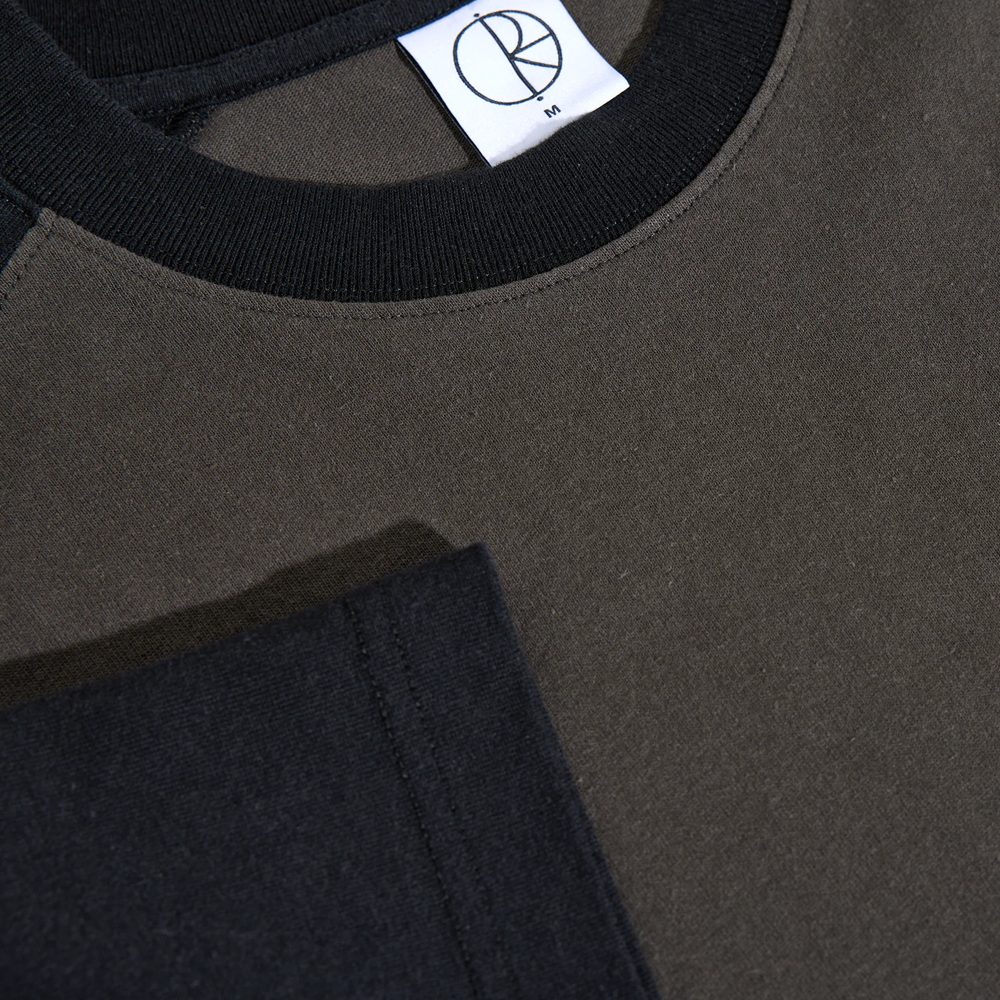 Close-up of the Polar Tee Doe Dirty Black Black, a color-blocked black and olive green cotton double jersey shirt with a black collar, white tag featuring an embroidered circular R logo, and visible stitching on the loose fit fabric.