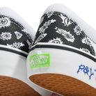 Close-up of two Punk and Yo x Vans Skate Slip On VN000EKPY281 Canvas Shoes, featuring black and white patterned canvas, a signature green Vans Off The Wall skateboarding logo on the heel, distinctive P&Y blue lettering on the white midsole above a gum outsole—part of the bold collaboration redefining skateboarding streetwear.