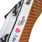 Here’s your rewritten sentence using the provided product data: Close-up of the Punk and Yo x Vans Skate Slip On VN000EKPY281 Canvas Shoe in white, featuring a brown rubber sole. This collaborative sneaker showcases black and red graphic designs and multilingual stylized text on the side—with details like a red heart—paying bold tribute to skateboarding streetwear culture.