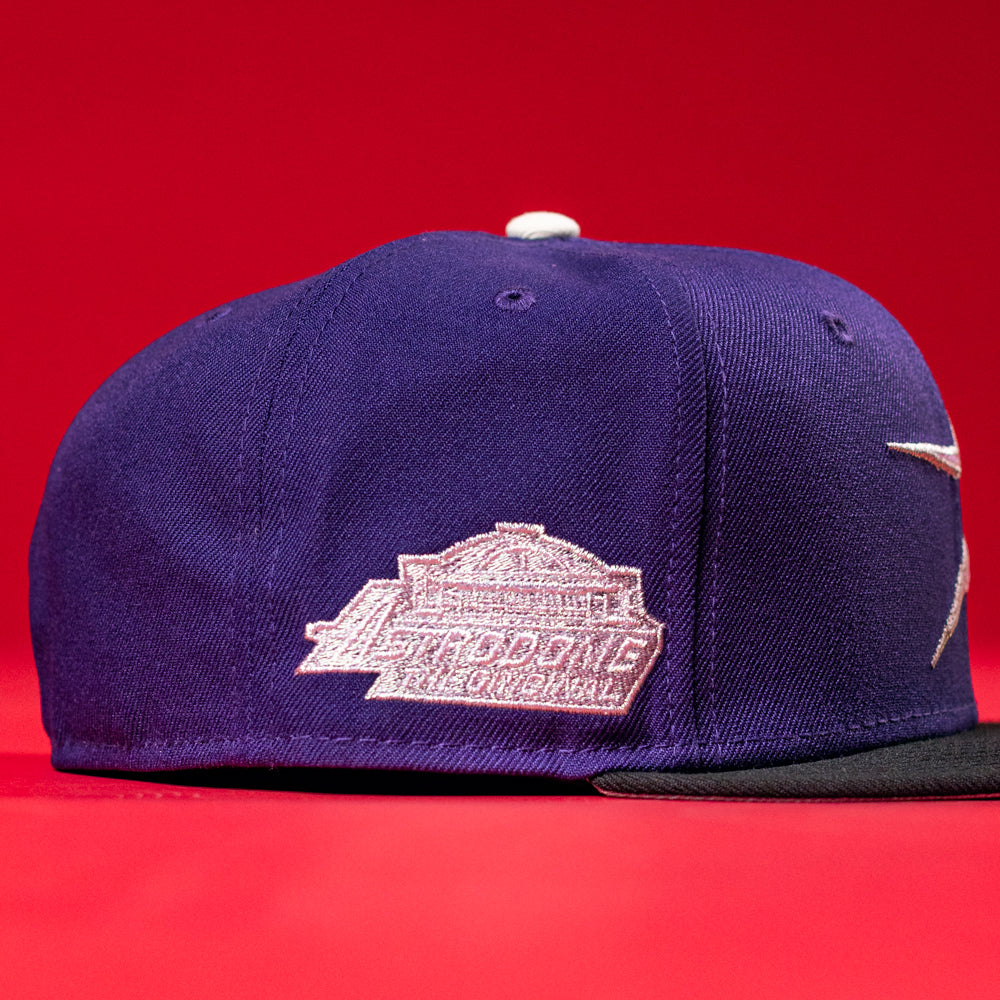 The De Uva New Era Purple Houston Astros 5950 Fitted Hat features a purple and black design with a white embroidered side logo, shown against a bright red background.
