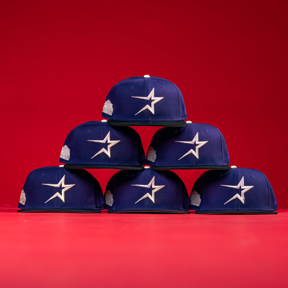 Six De Uva New Era Purple Houston Astros 5950 Fitted hats, each displaying the iconic star logo, are stacked in a pyramid formation against a vibrant red background.