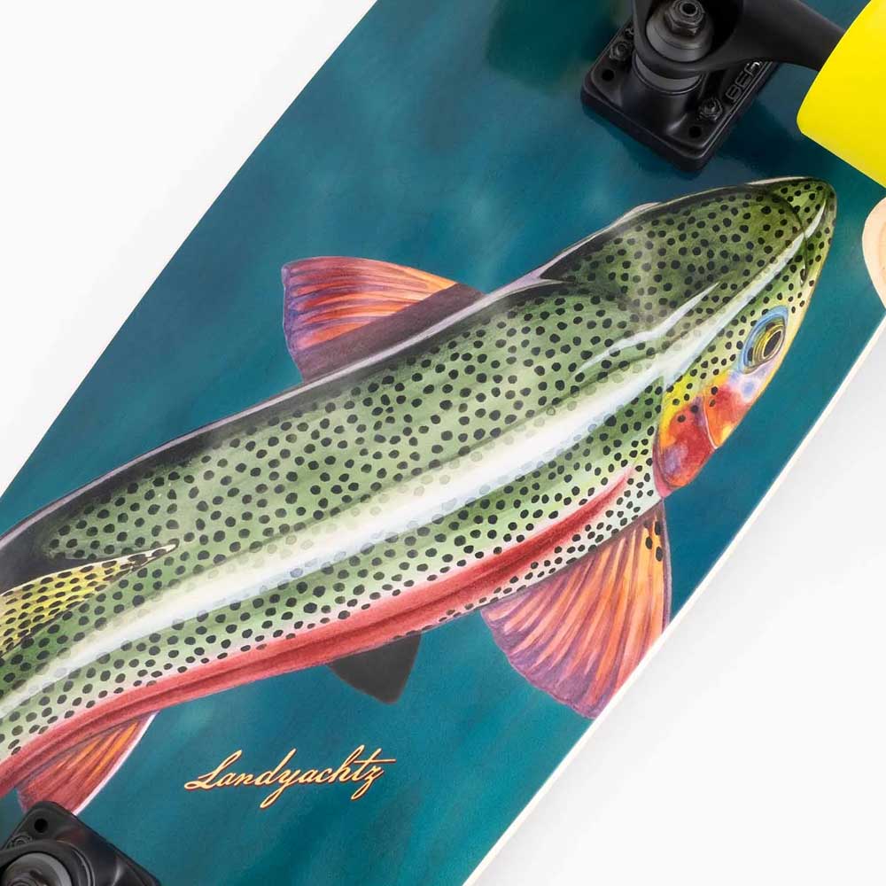 A close-up of the Raft Trout Landyachtz Complete Skateboard shows a wide cruiser deck with a realistic, colorful spotted fish illustration and "Landyachtz" scripted on the bottom left.