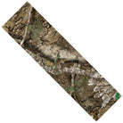 The Realtree APX Grip Tape 9in x 33in Sheet Graphic Mob Griptape, featuring a camouflage design with brown tree bark, green leaves, moss, and dirt, is shown diagonally against a white background.