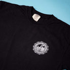 The Refinery Southside T-Shirt Black Cool Gray Tee by Bigo is a black tee with a white circular logo—skateboarder, text, and barbed wire—honoring Southside Skatepark. Displayed flat on a light blue background.