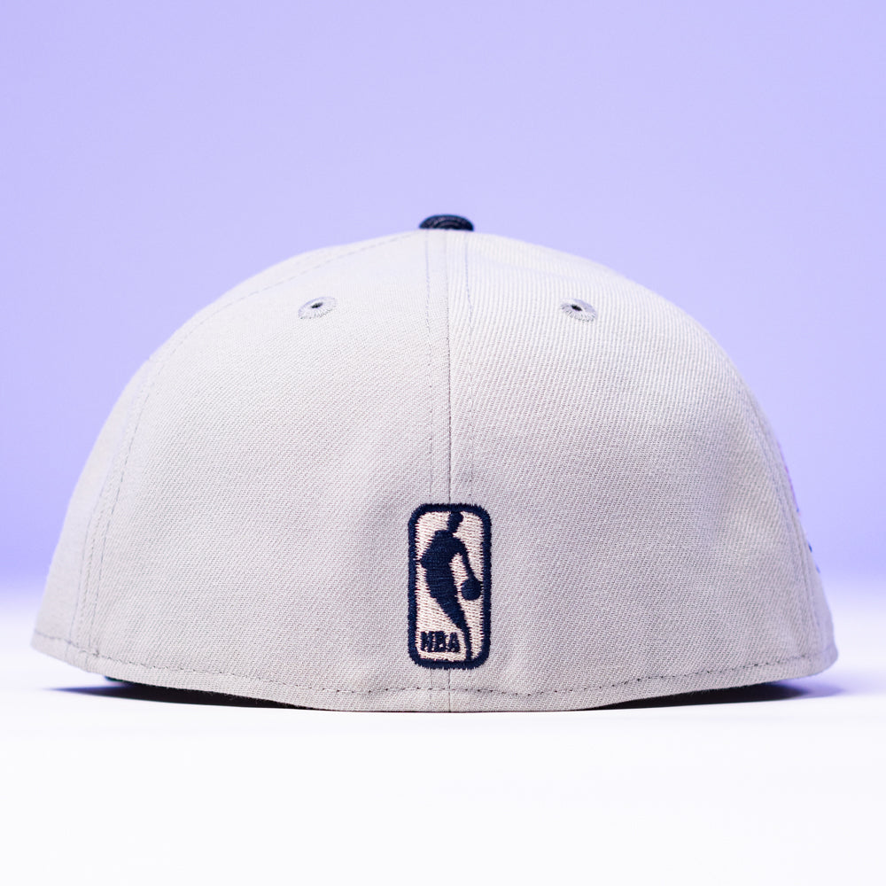 The Unit 95 ASG Denim Houston Rockets New Era Hat 5950 Fitted in light grey, shown from the back with a black NBA logo embroidered near the bottom center, set against a soft purple background. Inspired by the iconic New Era 95 ASG Hat.