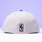 The Unit 95 ASG Denim Houston Rockets New Era Hat 5950 Fitted in light grey, shown from the back with a black NBA logo embroidered near the bottom center, set against a soft purple background. Inspired by the iconic New Era 95 ASG Hat.
