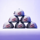 Six grey The Unit 95 ASG Denim Houston Rockets New Era Hat 5950 Fitted caps with vibrant embroidered logos are stacked in a pyramid against a purple gradient backdrop, highlighting their iconic style.