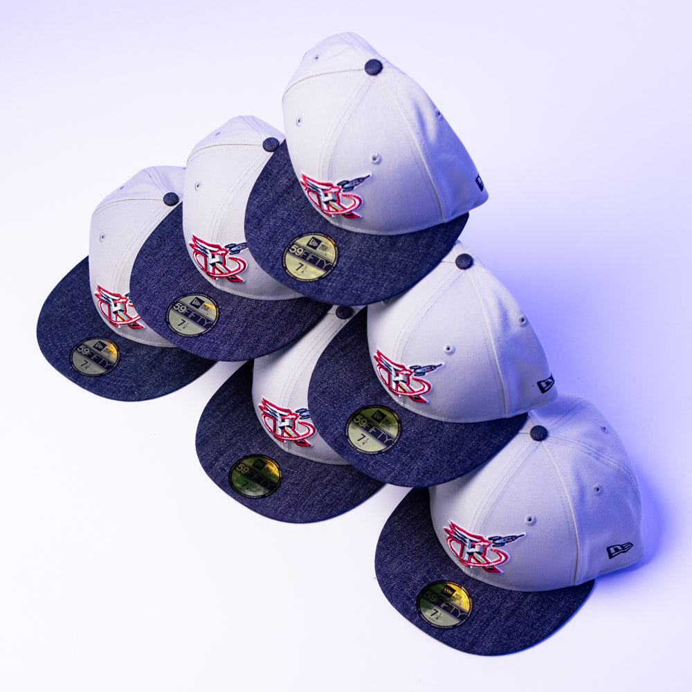 Six gray and navy blue The Unit 95 ASG Denim Houston Rockets New Era Hat 5950 Fitted caps, each with a red, white, and blue patch on the front and gold stickers on the brim, are stacked in a zigzag pattern on a white surface.