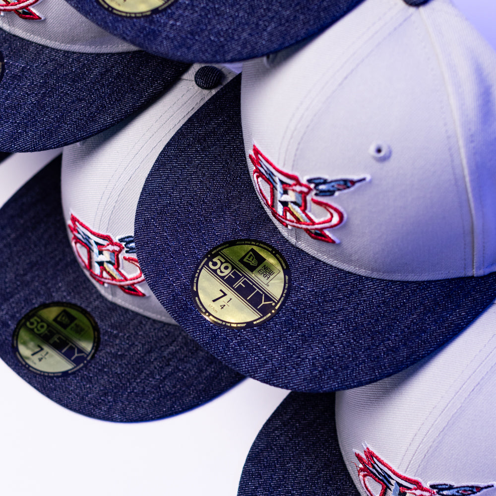 A close-up of stacked gray and blue The Unit 95 ASG Denim Houston Rockets New Era Hat 5950 Fitted caps, each with a red and blue embroidered logo and a gold size sticker on the brim showing size 7 1/4.