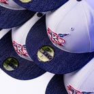 A close-up of stacked gray and blue The Unit 95 ASG Denim Houston Rockets New Era Hat 5950 Fitted caps, each with a red and blue embroidered logo and a gold size sticker on the brim showing size 7 1/4.