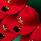 Multiple Rusty Screw OG Scarlet Copper Houston Astros New Era 5950 Fitted hats are arranged overlapping on a green surface in a close-up view. Each hat features a bright scarlet color, copper star logo, official stickers on the brim, and signature Astros detailing.