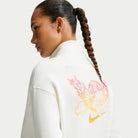 A woman with a long braided ponytail wears the Nike SB Skateboarding Sail IM5463133 1/2 Zip Fleece Crew, an imported white jacket with a pink and orange cherub graphic on the back; this stylish piece is also machine washable.