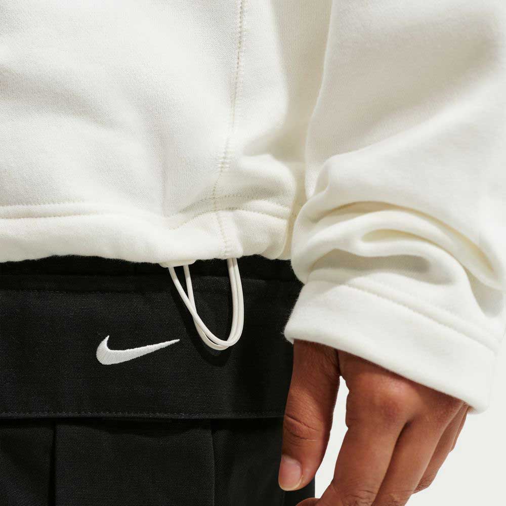A person wearing a Sail IM5463133 Skate 1/2 Zip Fleece Crew Nike SB Skateboarding top and black pants with a visible Nike logo, with part of their hand near the drawstring of the top.