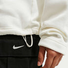A person wearing a Sail IM5463133 Skate 1/2 Zip Fleece Crew Nike SB Skateboarding top and black pants with a visible Nike logo, with part of their hand near the drawstring of the top.