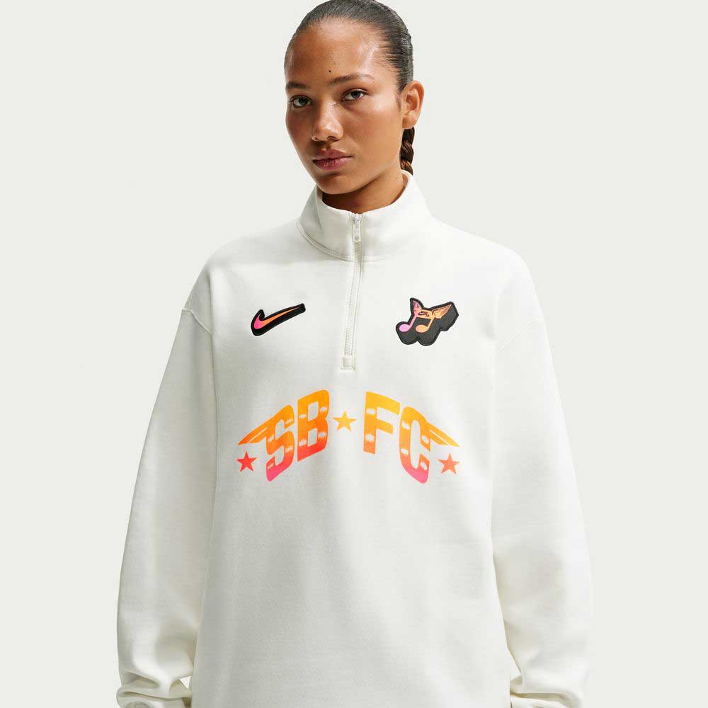 Someone wears the Nike SB Skateboarding Sail IM5463133 Skate 1/2 Zip Fleece Crew, featuring colorful graphics, a Nike logo, a dog face patch, and bold "SB-FC" with stars. This imported sweater is machine washable and shown against a plain light background.