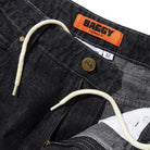 Close-up of Distressed Flat Black Relaxed Denim Jeans by Butter Goods, featuring a relaxed fit, internal drawstring waistband, visible zipper and button, an orange BAGGY Very Baggy Fit label, size 32 white tag, and made from 100% cotton.