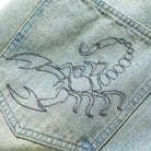 Close-up of the Scorpion Stitch Tinted Light Blue Denim Jeans by Butter Goods, featuring an embroidered scorpion on the patch pocket—ideal for those who love unique, baggy fit denim.