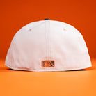 A Backlash Corpus Christi Hooks New Era 5950 Fitted Hat in white is shown from the back against an orange background, with a small orange and black rectangular patch near the bottom edge.
