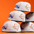 Six Backlash Corpus Christi Hooks New Era 5950 Fitted hats in white are stacked against an orange background, each featuring a Texas outline with a star and bat, plus an embroidered Texas League logo on the side.