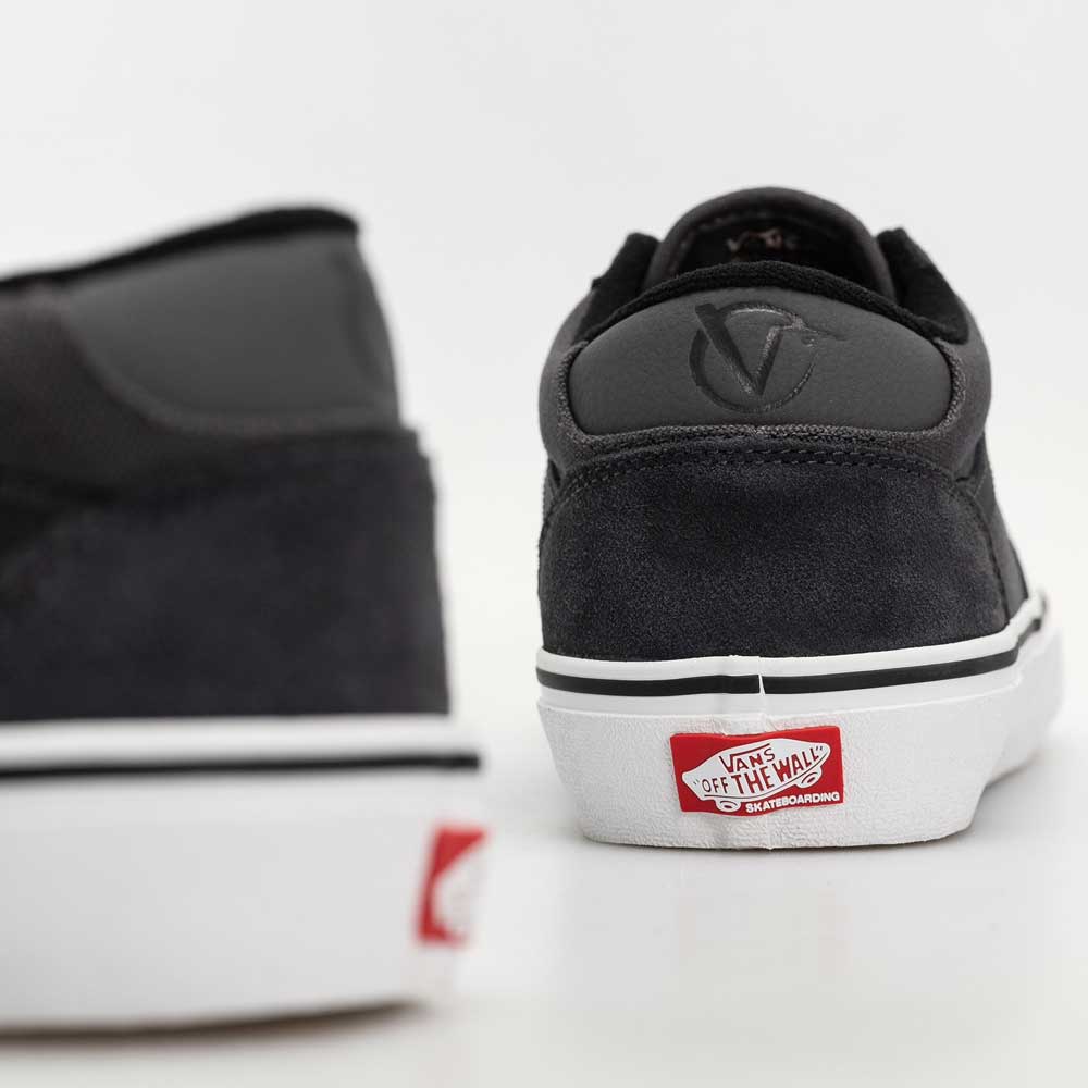 A close-up of two Skate Rowan Asphalt White VN0A5JICRP9 Suede Vans shoes highlights the black suede heel. The white sole displays the red Vans Off The Wall logo on the back, with one shoe in the foreground, slightly out of focus.